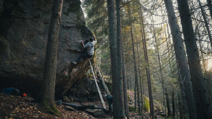 YouTuber Sam Lawson, the man behind Wedge Climbing, sends a tall granite boulder in a light-dappled Finnish forest