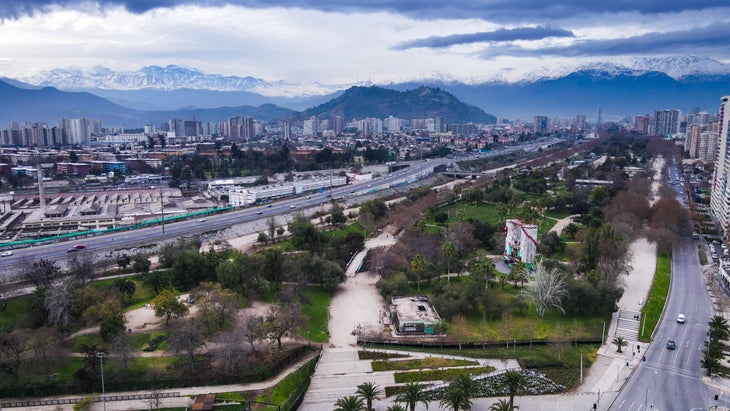 A view of Parque de Escalada Los Silos in a small park sandwiched between two highways, with big mountains in the distance above the city.