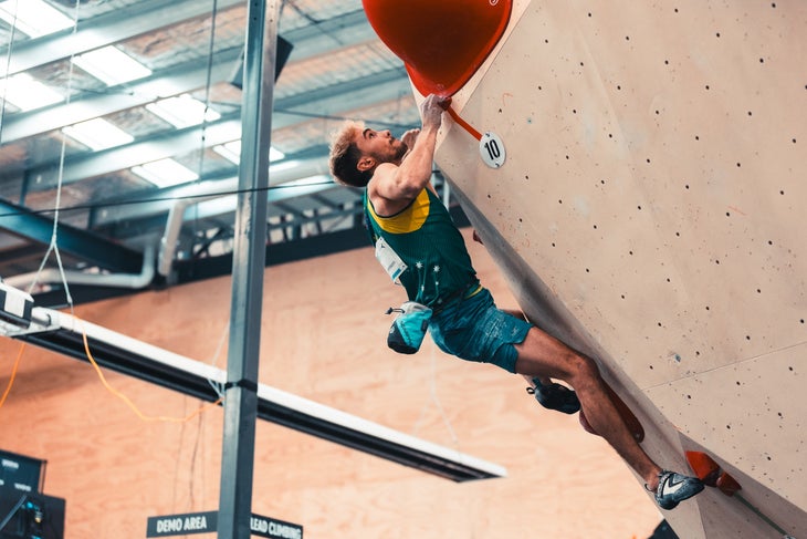 Olympic climber Campbell Harrison competes in an indoor bouldering competition wearing a blue tank top.