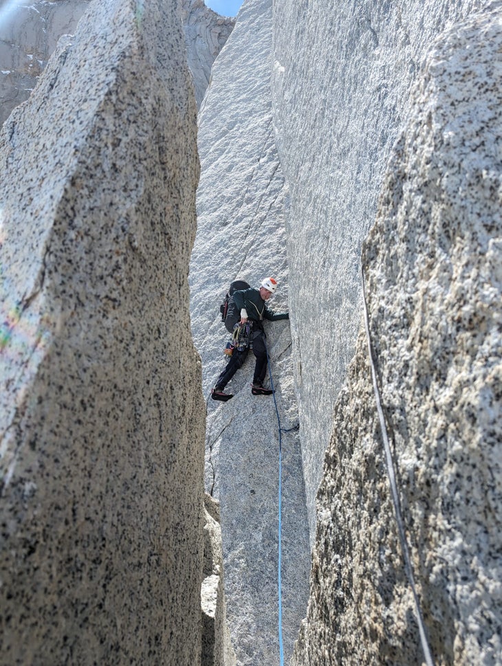Nat Bailey climbs a vertical granite crack in Patagonia while wearing a large backpack.