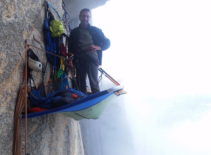 John Middendorf standing in a portaledge on a misty big wall climb