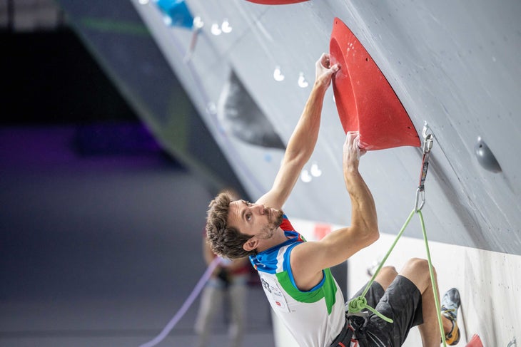 An Italian climber moving through a red volume on a lead route