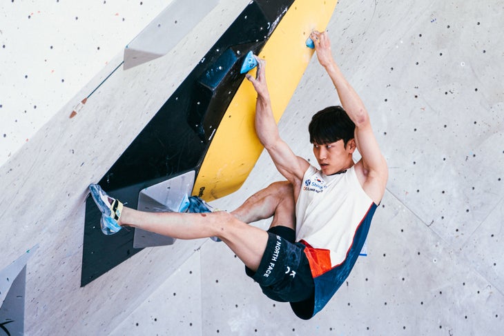 A male climber moving through a difficult crimp sequence on a steep bouldering wall.