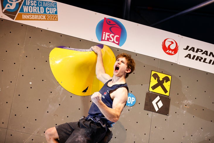USA's Colin Duffy celebrating at the top of a boulder problem—making a fist and shouting.