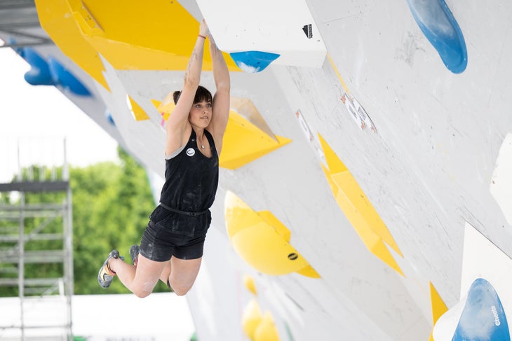 A female rock climbing performing a lache: a move where you hang from your hands and swing your body to generate momentum to the next holds.
