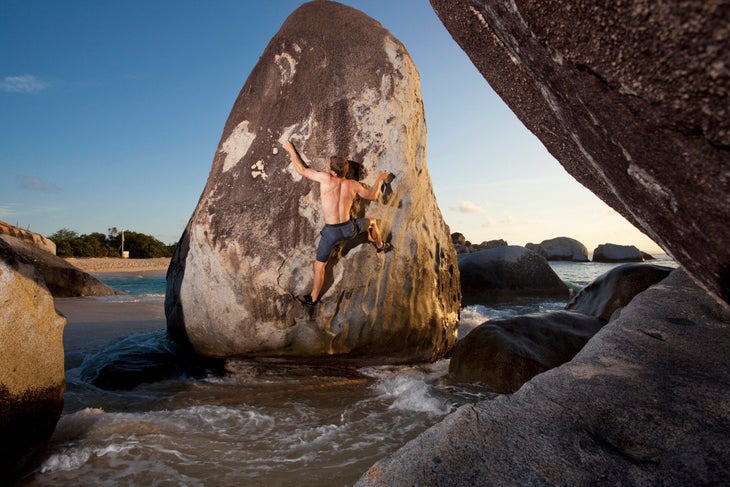 A male climber climbs a boulder near a beach at high tide in Virgin Gorda, the British Virgin Islands.