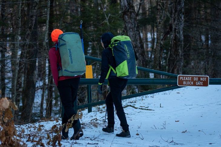 Two climbers walk past metal gate to access sport climbing area in New Hampshire.