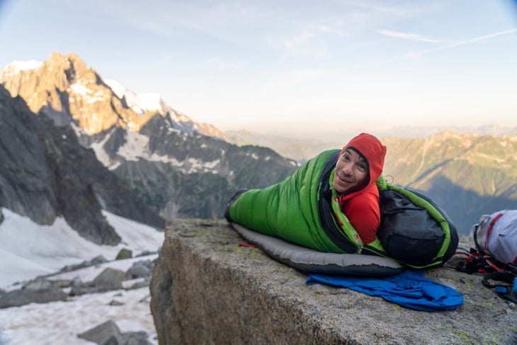 Alex Honnold in a sleeping bag on a rock in the alps.