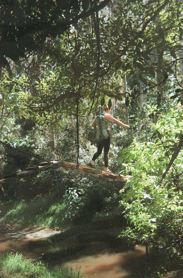 Woman walks through forest in Colombia carrying a climbing rope.