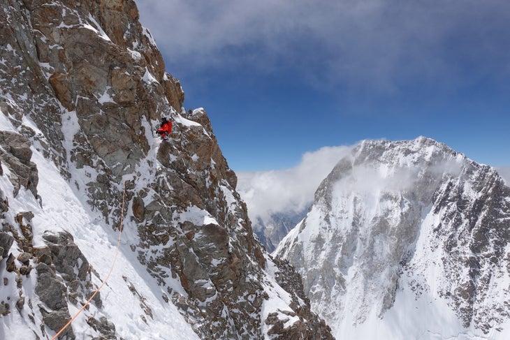 A climber in a red down coat paused on a steep cliff high on Gasherbrum III.