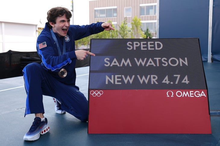 Sam Watson making a very Gen Z face as he points at a billboard of his own speed record