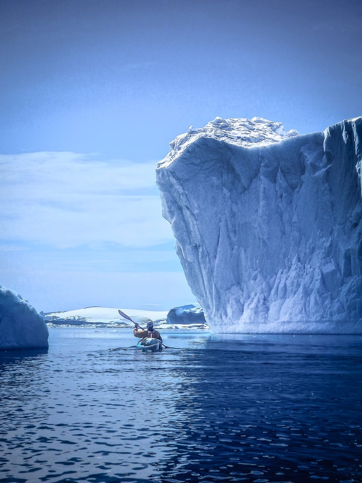 A kayaker paddles between tall, precarious icebergs in the Arctic.
