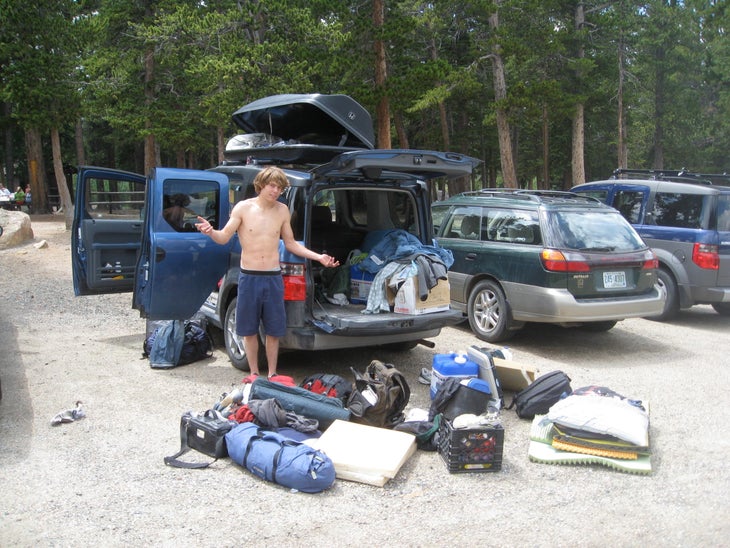 A climber standing beside a car with his gear strewn about the parking lot.