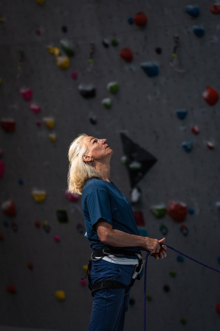 Jame Logan belays a climber in a dark gym.