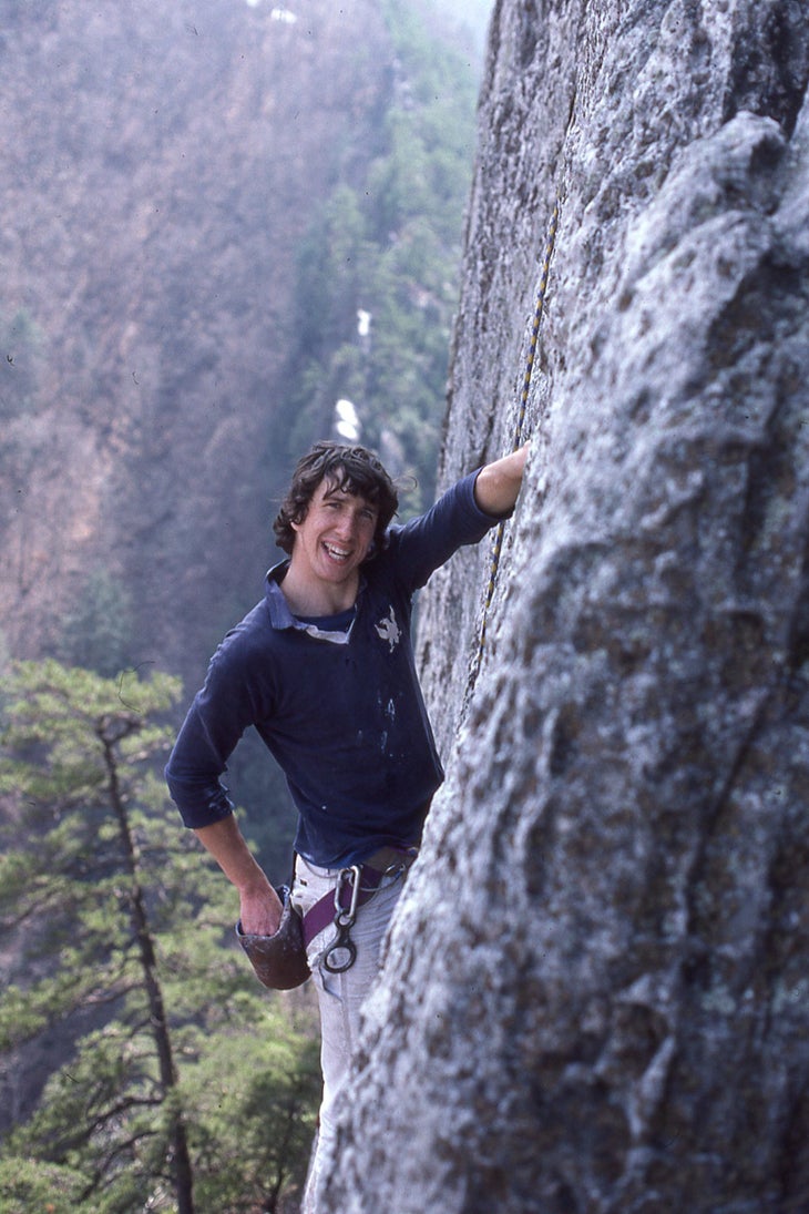 A teenage Russ Clune climbs at a crag in a forest.