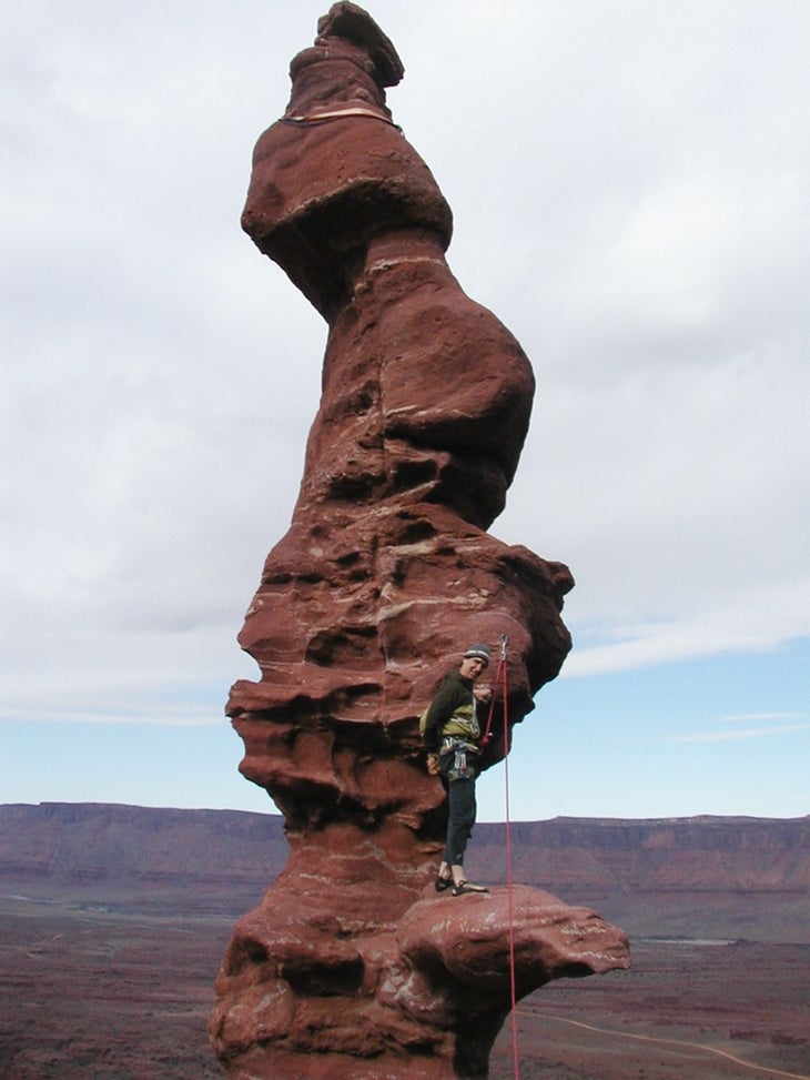 Russ Clune climbs a precarious sandstone tower on a cloudy day.