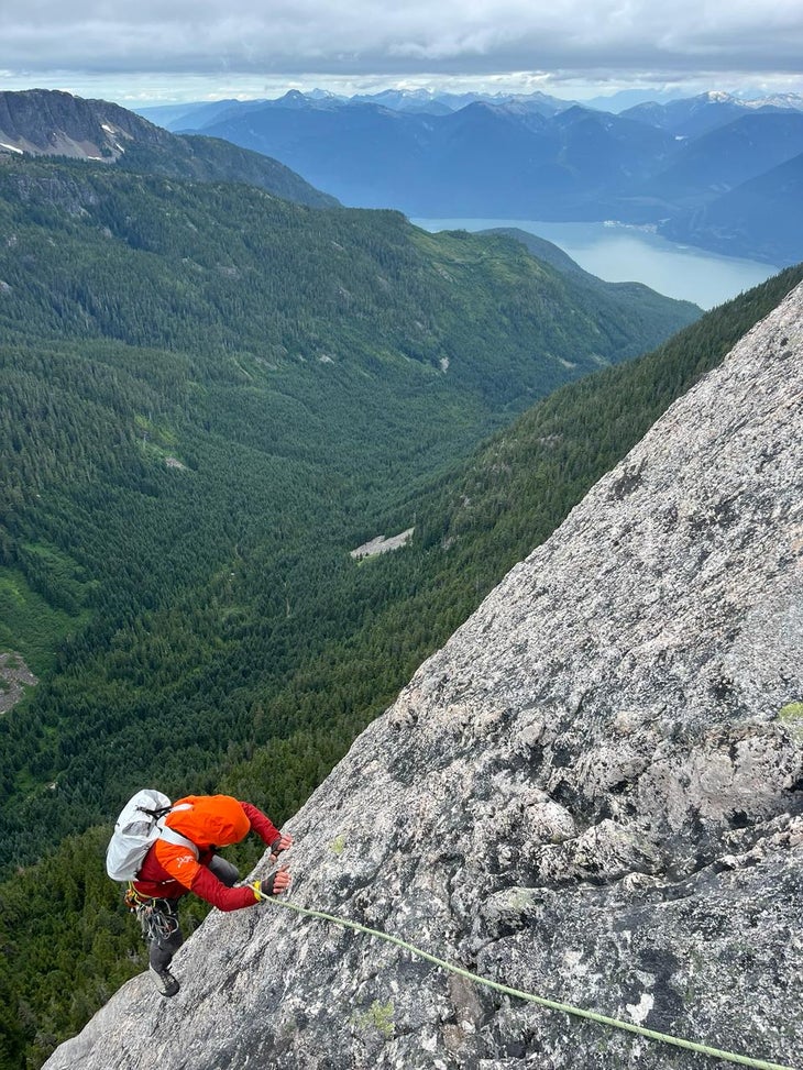 Man in red jacket climbs a granite slab on a sunny day in the mountains.