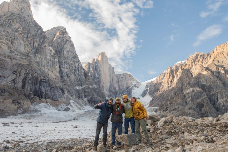 Four climbers smile in front of Greenland's Mirror Wal on a sunny day.