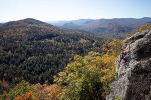 A woman climbing near the top of a cliff with excellent autumnal views of the White Mountains behind her.