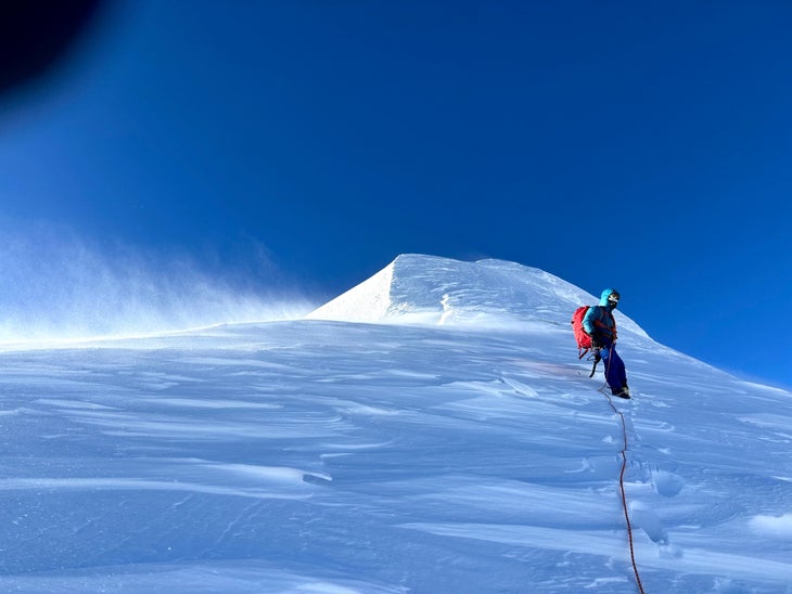 A climber on a wind-swept snowfield near the summit of Yashkuk Sar