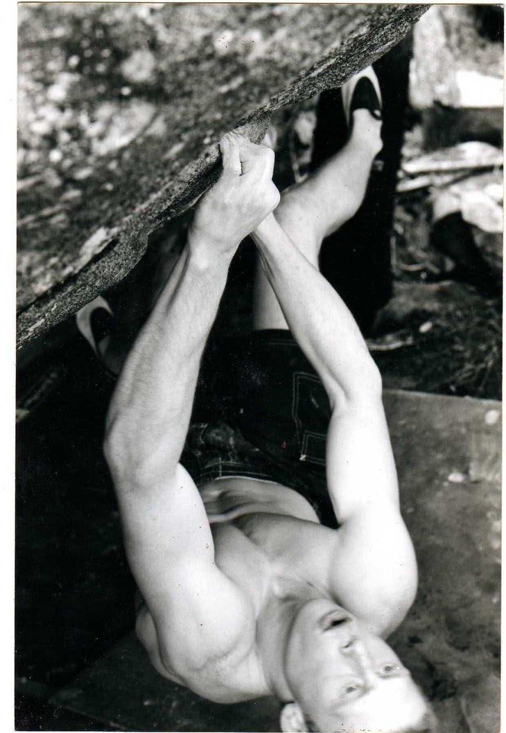A black and white photo of a young male climber—Johnny Goicoechea—on a steep, crimpy boulder problem.
