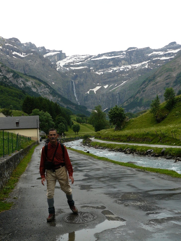 Javier Botella de Maglia walking beside a mountain stream with waterfalls pouring from the cliffs in the background.