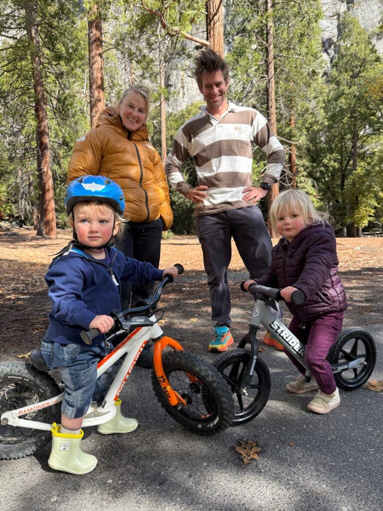 a woman and a man standing by two kids on striders