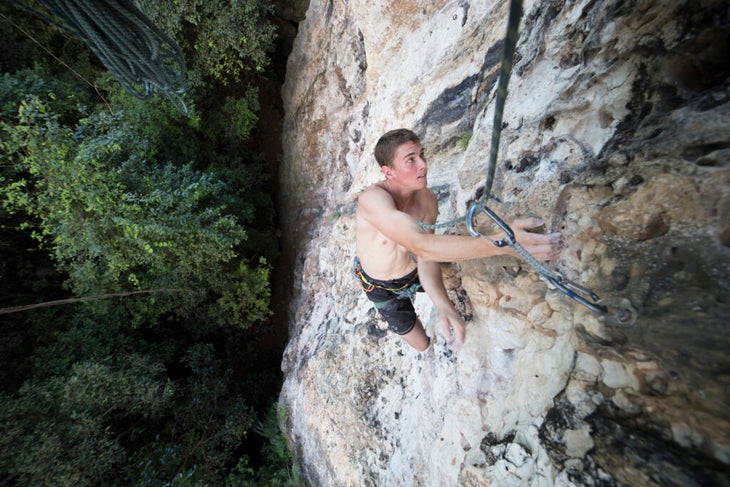 a male shirtless climber sport climbing with trees in the background