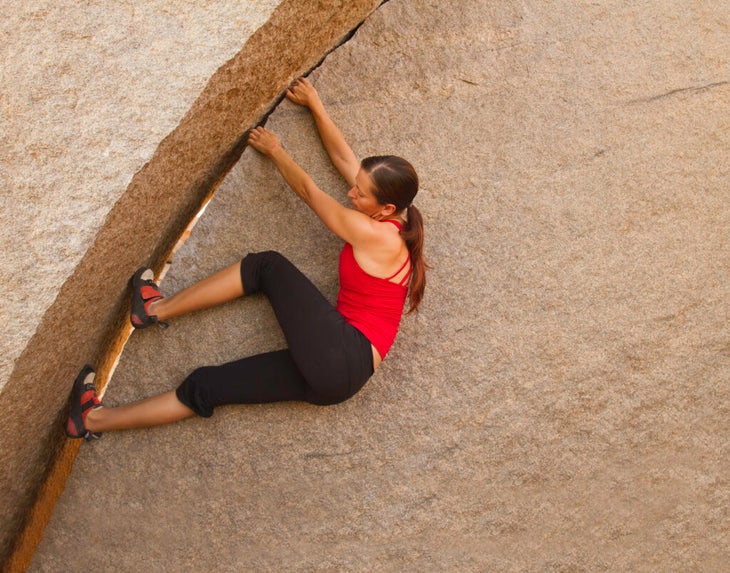 a woman in a red shirt and black pants laybacking on a boulder