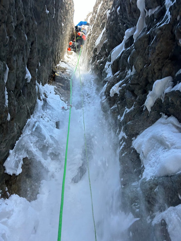 A climber ascends a steep rock chimney filled with ice.