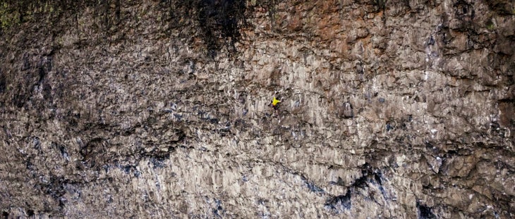 A panorama of a rock climb with a man climbing in the distance