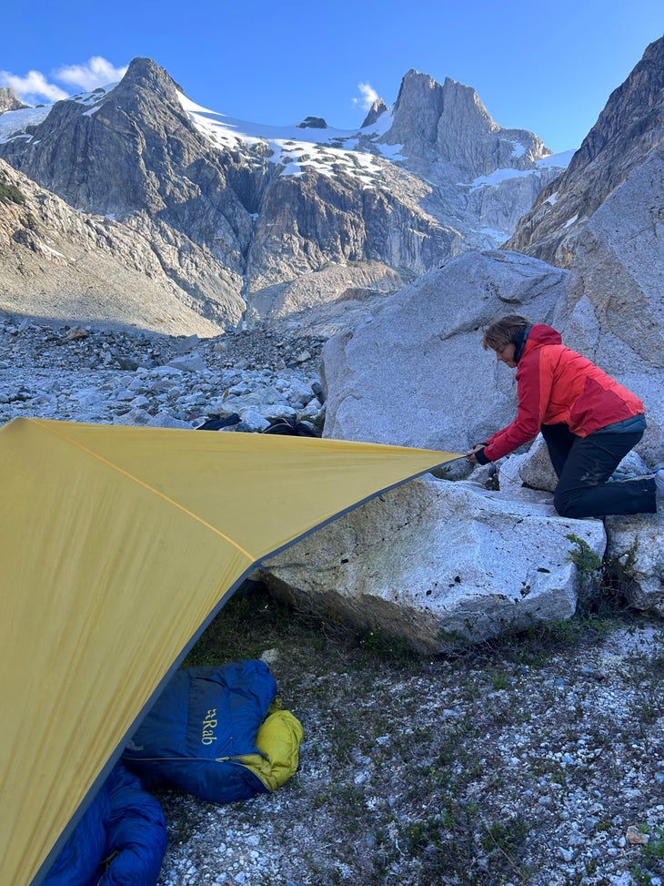 Woman in red jacket sets up tent in remote Patagonian valley at sunset.