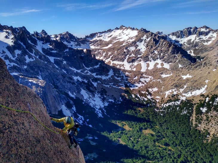 A person in a yellow jacket climbs a granite ridge on a sunny day in Patagonia.