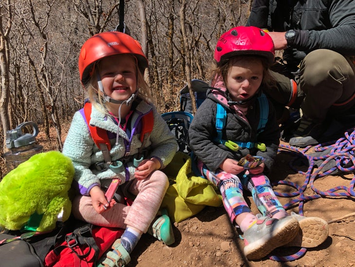 two toddlers wearing helmets sitting in dirt