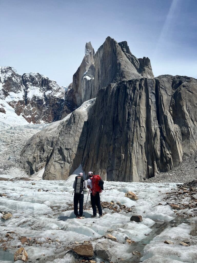 two climbers stand in snow before a giant tower