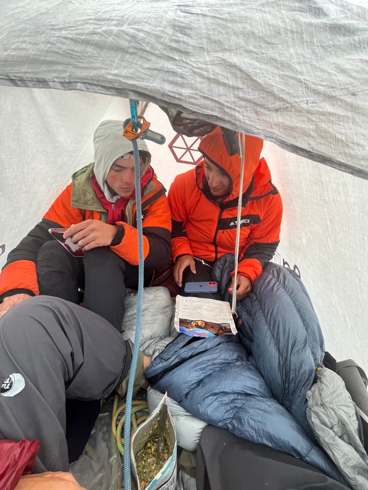 Three climbers squeeze in a small white tent in the mountains.
