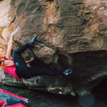 Young rock climber woman heel hooks on a cliff rock at the coast with safety mats