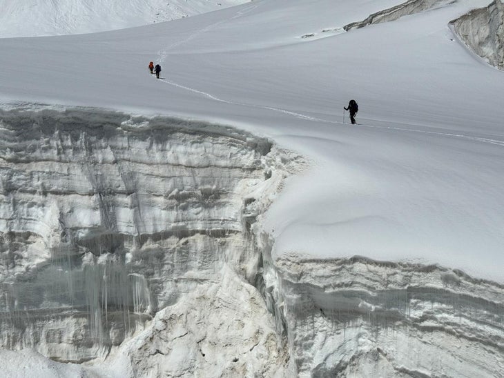 Two climbers traverse a snowy glacier covered in crevasses.
