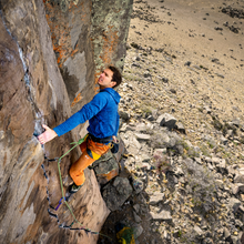 A man scales a vertical cliff face in one of the best climbing harnesses of 2026