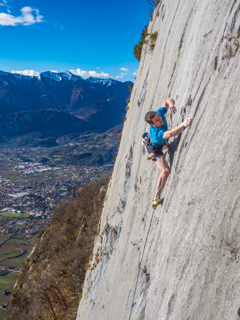 Adam Ondra in a blue shirt climbing a bare face of slab