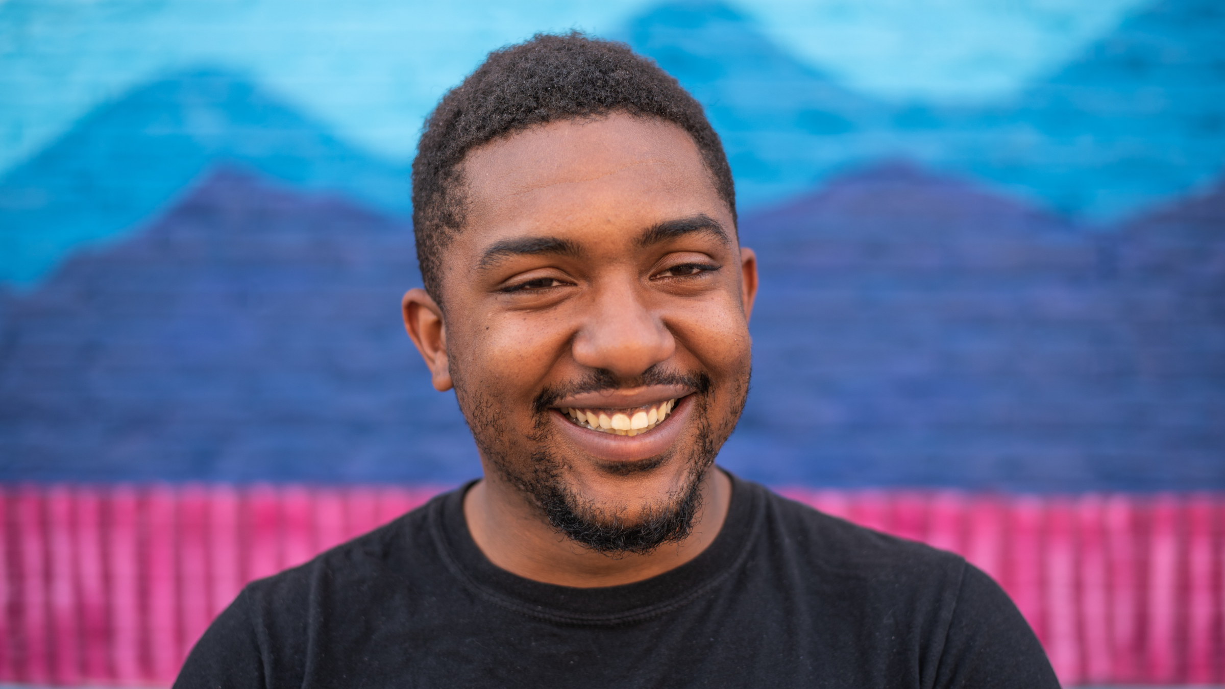 Climber Jarmond Johnson, seen here smiling in black T-shirt in front of blue and pink mural, died on June 29, 2025