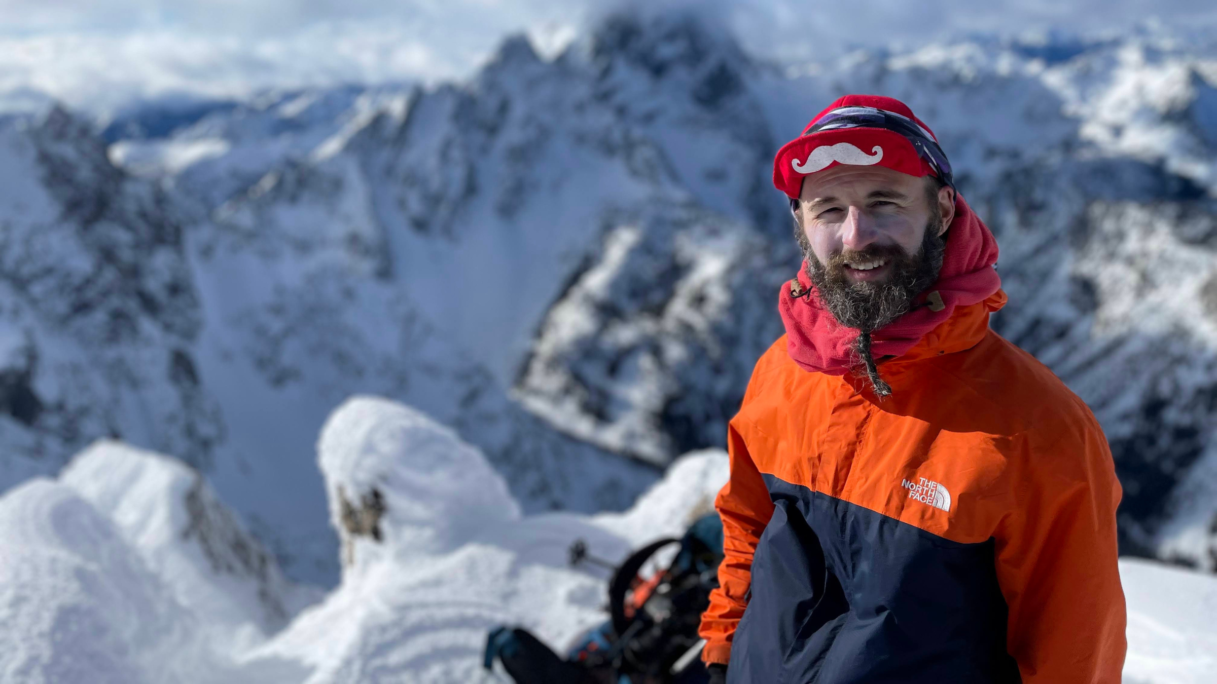 Climber Ross James Wallette, seen here at the top of snow-covered mountains in an orange and black jacket and red hat, died on August 18, 2025
