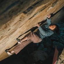 A woman in a blue jacket climbs an overhanging boulder at night