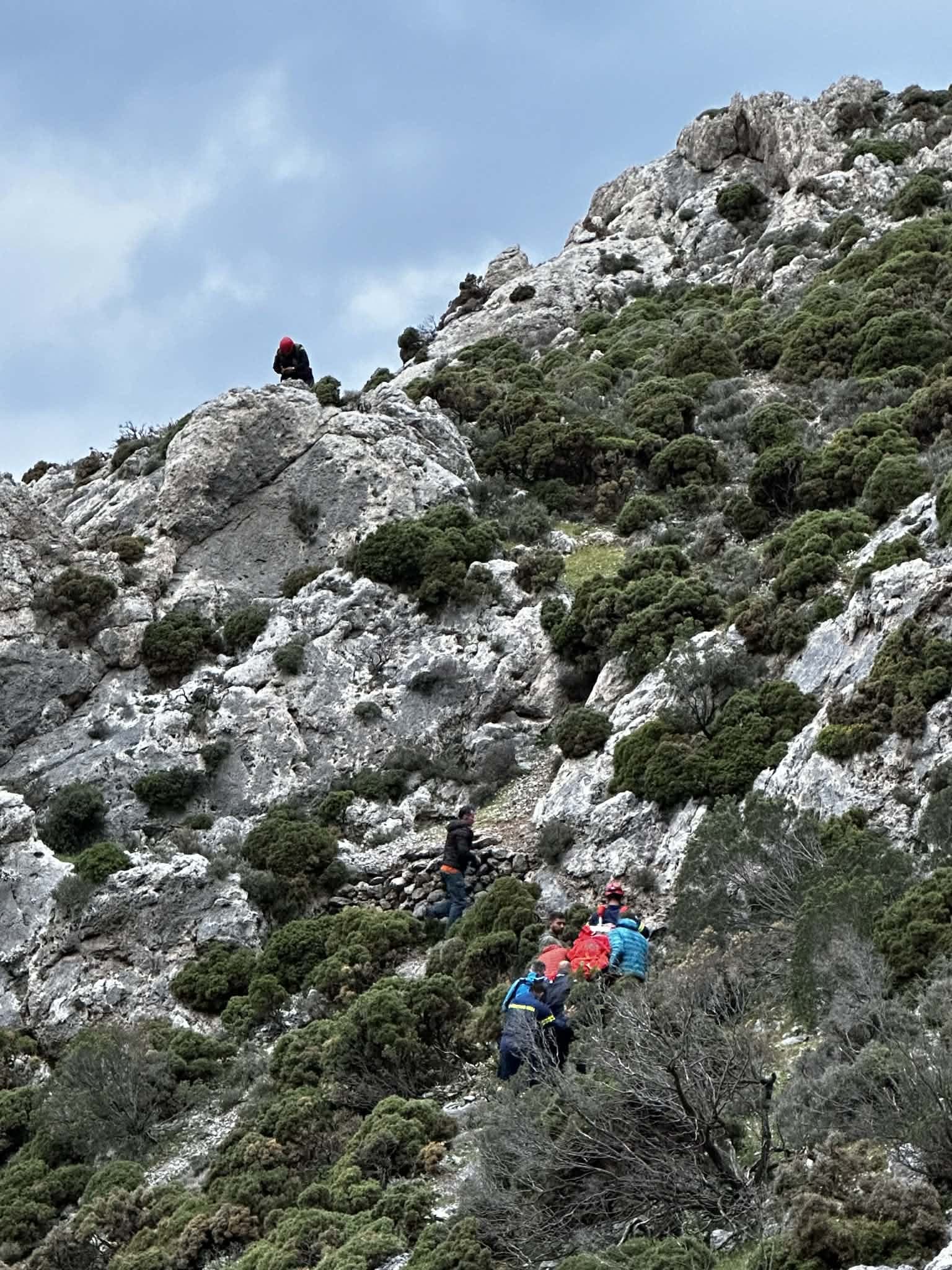 Rescuers carry a stretcher down a steep hillside.
