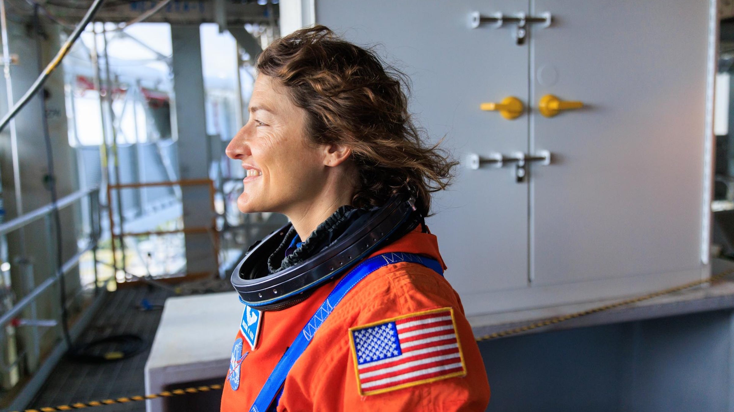 Christina Koch the climber: The astronaut climbs rock and ice on earth. Here she stands and looks out in an orange space suit.