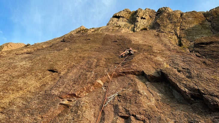 A climber ascends the face of a wall with hanging climbing rope in view