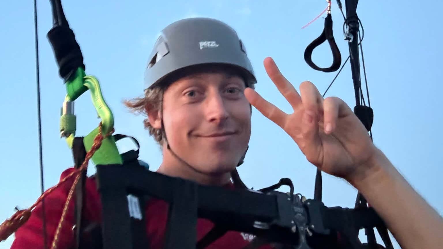 Matthew Clark poses with a peace sign while flying his paraglider