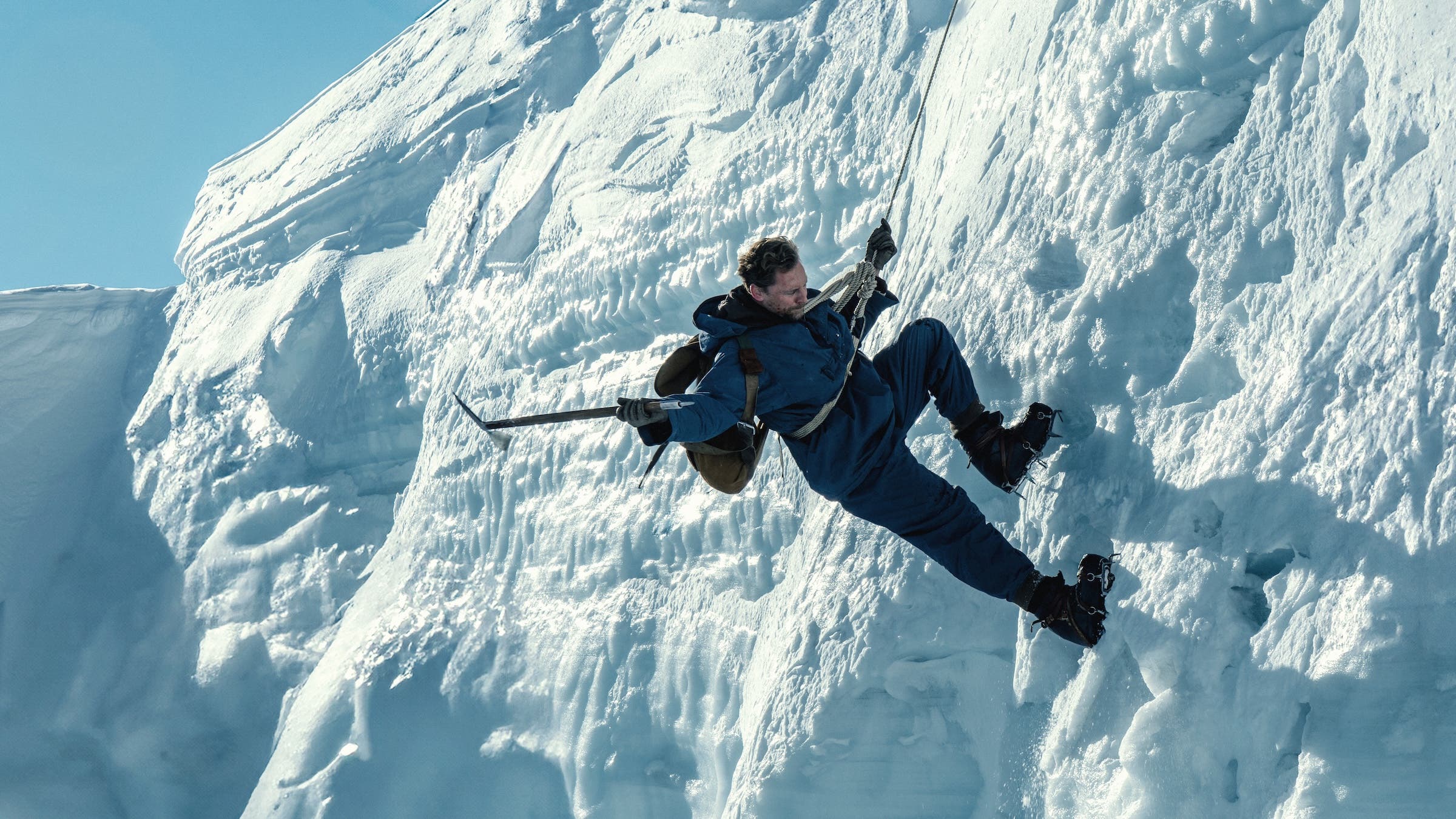 Tom Hiddleston being lowered from a rope with an ice axe